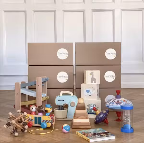 Leksakslådor från DearBaby fyllda med utvecklingsleksaker för bebisar och småbarn. Babyboxprenumeration med sensoriska leksaker, motoriska leksaker och Montessori-inspirerade material utspridda på golvet.