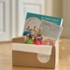 Den 3 månader långa babyboxen från DearBaby står öppen på golvet, fylld med baby- och barnleksaker som stöder motorisk utveckling och sensorisk lek.