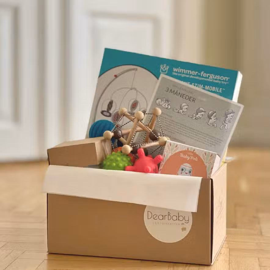 Den 3 månader långa babyboxen från DearBaby står öppen på golvet, fylld med baby- och barnleksaker som stöder motorisk utveckling och sensorisk lek.