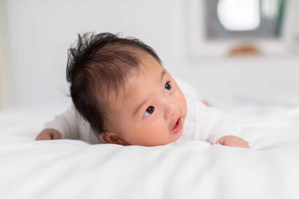 Nyfödd bebis 3 månader som ligger på magen och utvecklar nackkontroll .tummy tid för att stärka barnets nacke och axelmuskler.söt spädbarn som ligger krypande på vit säng lycka och kul. Mage tid. magtid blogginlägg om krokig skalle